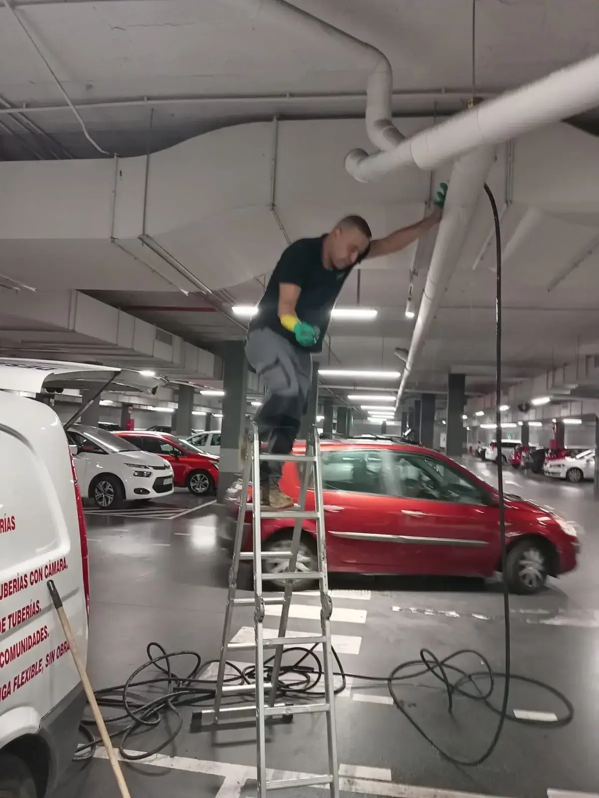 Operario de fontanería realizando la limpieza de tuberías aéreas en un garaje comunitario de Madrid