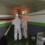 Operarios de fontanería con trajes de protección trabajando en tuberías de un sótano en Madrid